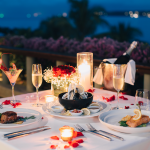 Tempat makan malam romantis dengan steak, seafood, dan sampanye, di teras yang menghadap laut pada malam hari.